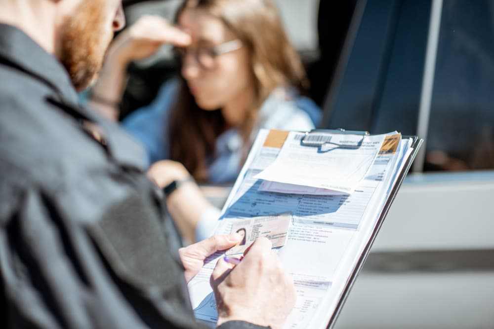 A policeman issues a fine to a young woman driver for traffic rule violations, with the focus on the folder in the officer's hands.