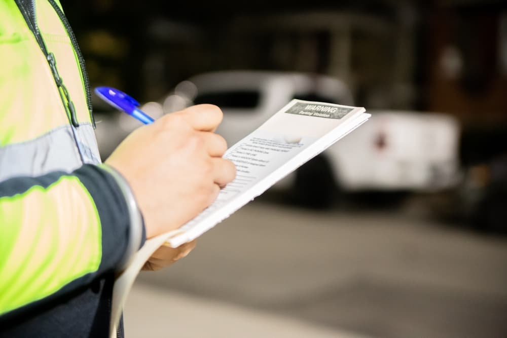 A security guard is issuing a parking ticket for a vehicle illegally parked on the street.