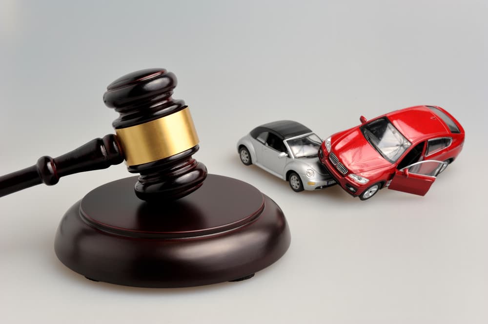 A judge's gavel with models of cars representing a car accident, arranged on a gray background.