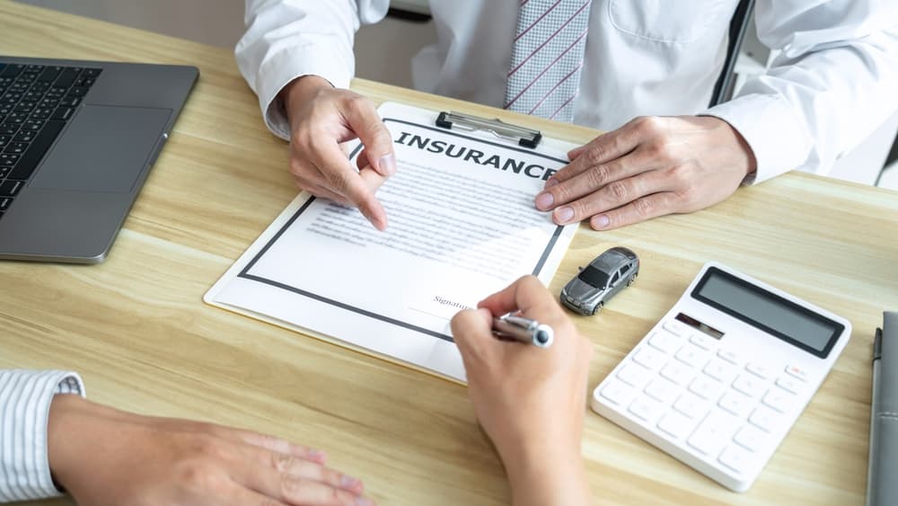 A car dealer manager presents a customer signing the car contract agreement.