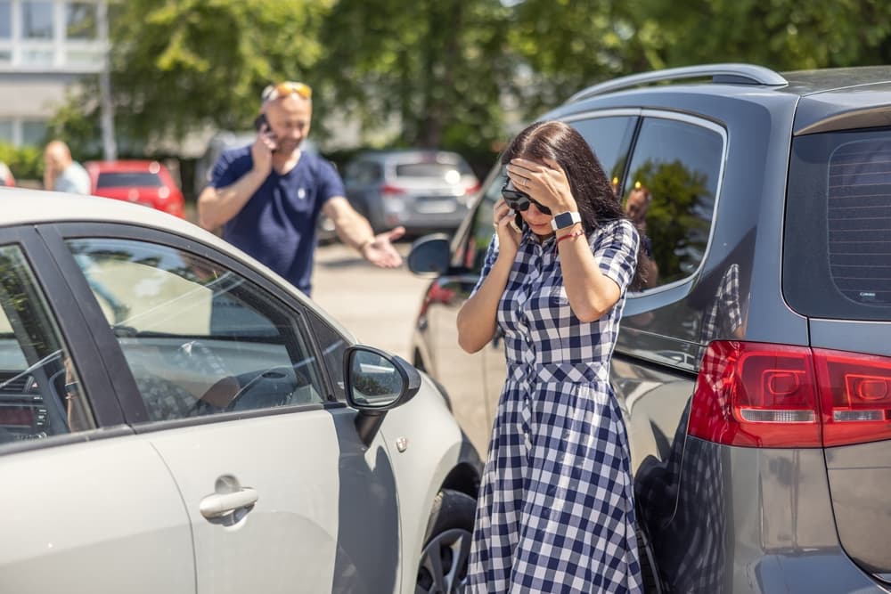 A frustrated woman, who scratched a man's car, talks on the phone while the angry man calls the police in the background.