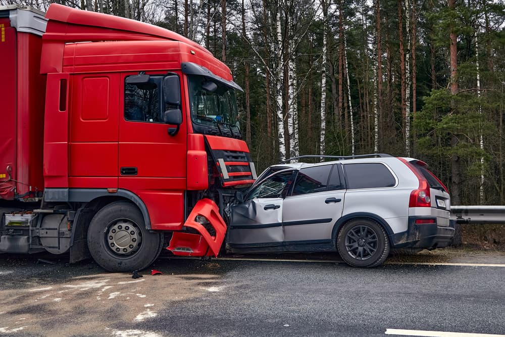 A car damaged after colliding with a heavy truck, set against a transportation-themed background.