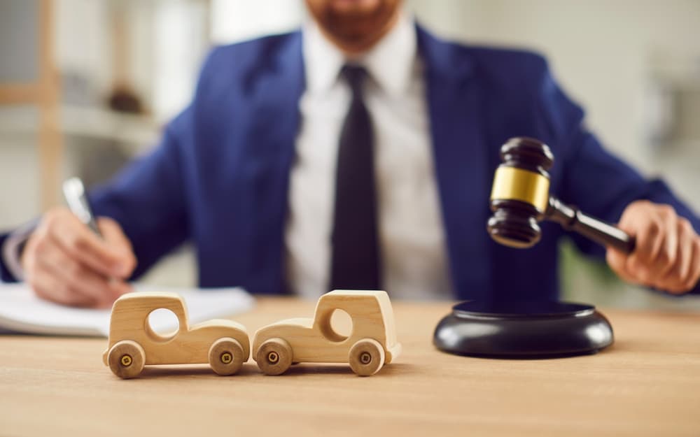 A car accident lawyer's desk with wooden toy crashed cars, a gavel, and documents related to fair compensation for injury, disability, and financial claims for traffic accident victims.