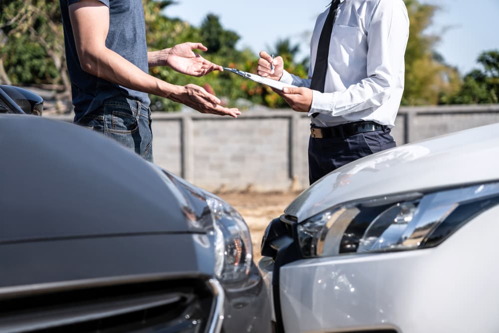 An insurance agent reviewing a car crash, with the customer negotiating, verifying, and signing the claim report after a collision.
