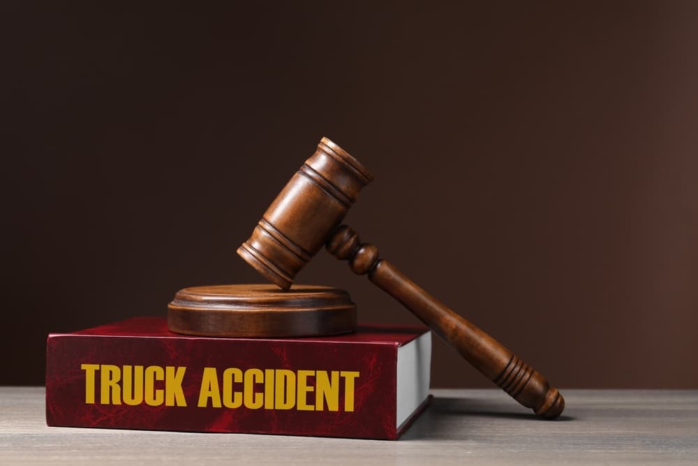 A truck accident law book and a judge's gavel placed on a wooden table, set against a brown background, symbolizing legal authority and justice.