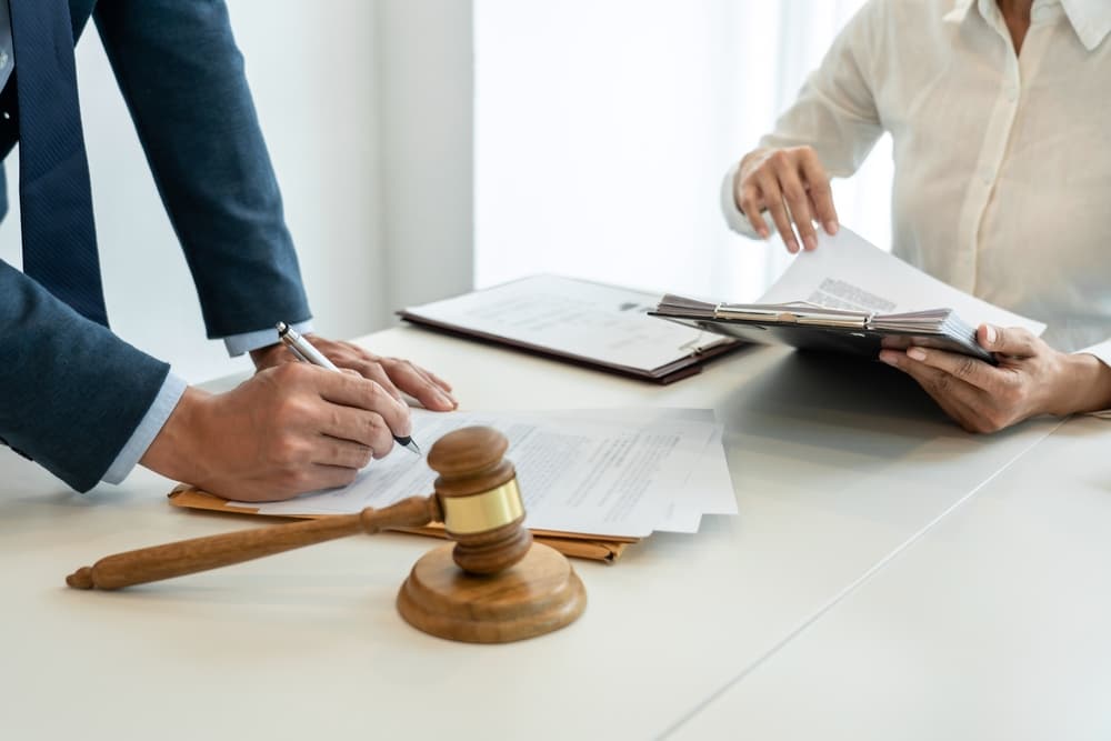 A male lawyer points to a legal document, explaining consultation terms and conditions to a businesswoman before she signs a contract at the law firm.