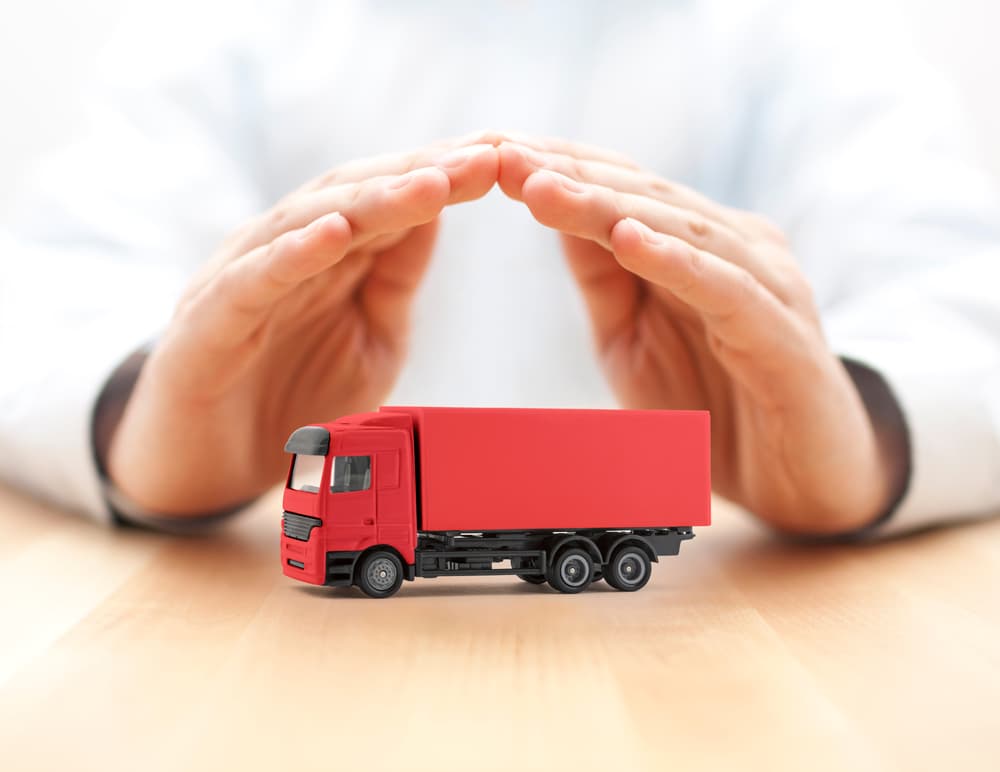 Hands shielding a red cargo delivery truck. The concept of truck insurance.