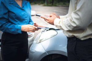 Individuals involved in a car accident use a mobile app to exchange contact information while awaiting the insurance agent.