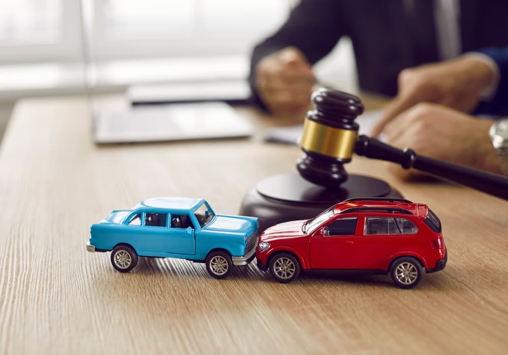 Miniature crashed cars on a courtroom table with a gavel, symbolizing legal services, civil court trials, vehicle accident cases, and insurance claims.