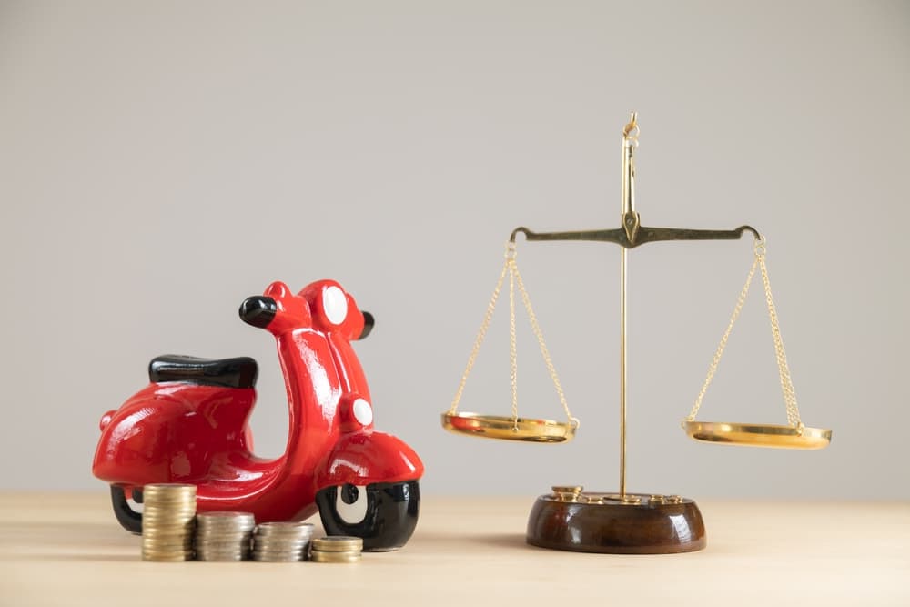 Close-up of a yellow motorbike piggy bank with scales and money, symbolizing car insurance savings and vehicle accident coverage.