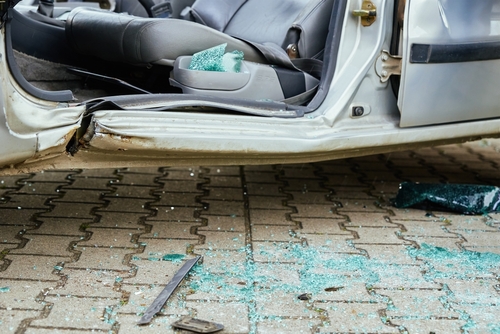 Side view of a damaged car with a shattered door and broken glass scattered on the pavement after an accident.