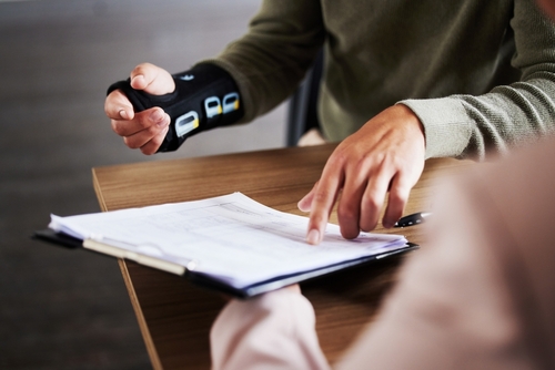 Injured person wearing a wrist brace reviewing and pointing at legal documents during a meeting, likely discussing a personal injury claim.