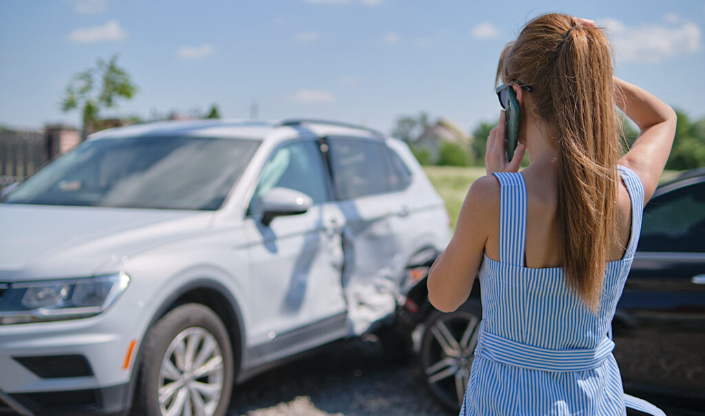 Stressed driver talking on cellphone on roadside near her smashed vehicle calling for emergency service help after car accident in Georgia.
